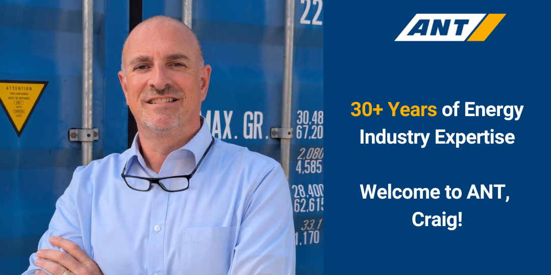 Portrait of Craig in a light blue shirt with glasses hanging from his collar, standing in front of a blue energy facility backdrop and ANT branding reading 'Welcome to ANT, Craig!'